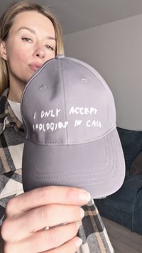 Cappello grigio con visiera curvata, caratterizzato da testo bianco che dice: "ACCETTO SOLO SCUSE IN CONTANTE." Materiale in cotone con dettagli di cucitura.