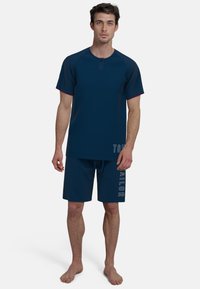 Conjunto de camiseta de manga corta y pantalones cortos azul marino con un cuello abotonado y un ribete de contraste en las mangas. Texto "TOM TAILOR" en los pantalones cortos en blanco.