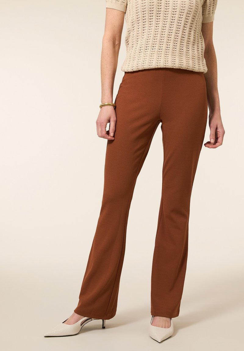 Bruine uitlopende broeken van zacht materiaal, met een gladde textuur, gecombineerd met witte puntige hakken voor contrast.