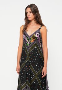 Vestido preto sem mangas com decote em V, adornado com padrões florais e desenhos geométricos em várias cores; material leve, com forma fluida.