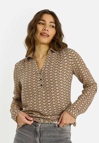 Camisa abotonada con un estampado geométrico en marrón, amarillo y blanco. Mangas largas con cuello, fabricada en una tela ligera.