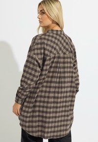 Camicia oversize a quadri marroni con maniche lunghe, polsini abbottonati e orlo arrotondato. Realizzata in tessuto morbido, presenta una vestibilità rilassata e un goccio posteriore.