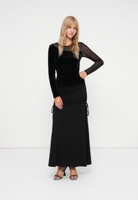 Black dress featuring a velvet bodice with long sheer sleeves, and a fitted skirt with side ties. Smooth texture with a flowing silhouette.