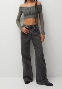 Top court gris décolleté avec un design froncé, associé à un jean noir ample taille haute et des chaussures noires pointues.