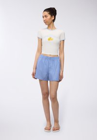 T-shirt bianca a maniche corte con bordino azzurro, con testo "AMALFI COAST" e grafica di limone; abbinata a pantaloni corti a righe blu e bianche.