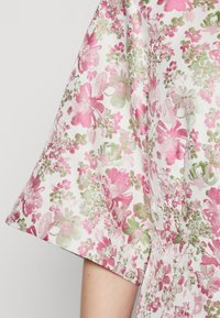 Blumenkleid mit kurzen Ärmeln, aus einem strukturierten weißen Stoff mit pinken und grünen Blumenmustern, der einen lebendigen, gemusterten Effekt bietet.