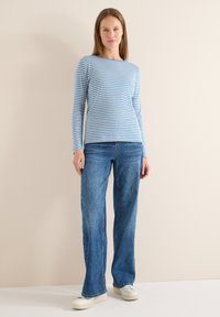 Chemise à manches longues rayée bleu et blanc, associée à un jean évasé bleu. La tenue présente des textures contrastées et un design décontracté.