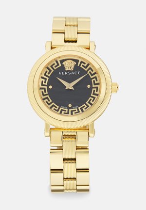 Orologio dorato con quadrante nero, bezel decorato e logo di un leone. I bracciali sono lucidi; presenta indici a bastone e due lancette.