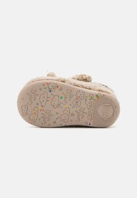 Chausson beige avec une texture duveteuse et une semelle en caoutchouc, arborant des motifs de nuages colorés et du texte. La semelle est plate avec une légère adhérence.