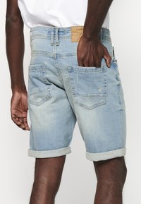 Shorts en denim bleu clair avec un ourlet retroussé, dotés de deux poches arrière, d'un délavage subtil et d'une étiquette en cuir avec logo à la taille.