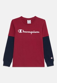 Rød langermet T-skjorte med marineblå ermer, med en hvit "Champion"-logo på forsiden og en liten logo på ermet. Laget av bomull.