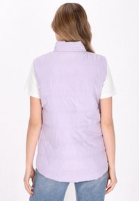 Lavendel Pufferweste mit hohem Kragen, horizontalen Nähten und einer glatten, glänzenden Textur. Getragen über einem weißen T-Shirt.