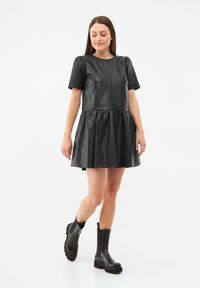 Musta nahkamekko lyhyillä hihoilla, istuva yläosa ja kerrostettu hame. Yhdistetty mustiin nilkkureihin, joissa on paksu pohja.