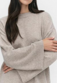 Jasno beżowy sweter wykonany z miękkiego dzianiny, z okrągłym dekoltem i szerokimi rękawami z prążkowanymi mankietami, prezentujący luźny krój.