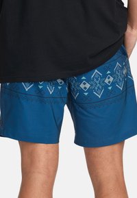 Shorts de bain bleus avec des motifs géométriques en bleu clair et noir. Conçus avec une taille élastique pour plus de confort.