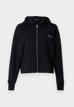 Sudadera corta negra hecha de tela suave, con cremallera completa, bolsillos frontales y un pequeño logo blanco bordado en el pecho.