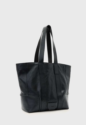 Czarna skórzana torba typu tote z podwójnymi paskami na ramię i subtelnym fakturowanym wzorem, stojąca pionowo na jednolitym szarym tle.