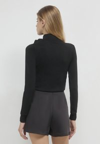Top lungo nero a maniche con una finitura testurizzata, dotato di un colletto alto e un accento arricciato sulla spalla. Abbinato a pantaloni corti neri.