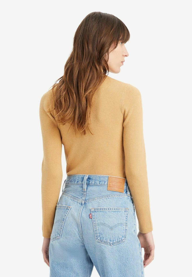Haut à manches longues côtelé moutarde associé à un jean taille haute bleu clair avec une pièce en cuir et deux poches arrière.