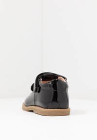 Czarne lakierowane buty z zaokrąglonym czubkiem, z rzepem i beżową gumową podeszwą. Gładka tekstura z minimalnymi akcentami.