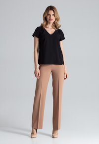 Zwarte V-hals top met korte mouwen, gecombineerd met beige rechtlopende broek en nude hakken op een lichtgrijze achtergrond. Glad stoftextuur.