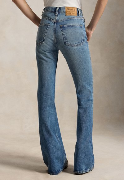 Inimene, kes kannab siniseid teksapükse, mis on alt laienevad ja millel on tagataskud ning vöökohal Polo Ralph Laureni nahast kaubamärgi märk.