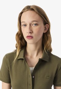 Polo shirt verde oliva con tessuto strutturato, maniche corte e bottoni sulla chiusura. Presenta un logo ricamato discreto sul petto.