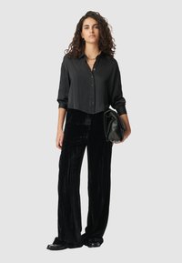 Czarna koszula z guzikami o luźnym kroju, w zestawieniu z szerokimi spodniami z czarnego aksamitu o fakturze. Dodatkiem jest kopertówka.