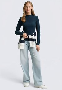 Meresinine soonikkoega pikkade varrukatega top koos helesiniste laiade pükstega. Vööl on seotud valge ja meresinise triibuline kampsun. Valged tossud.