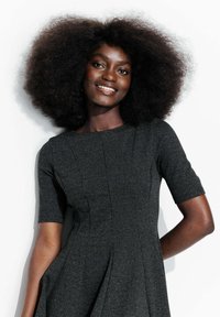 Robe ajustée à manches courtes en tissu texturé gris foncé, avec une jupe plissée et un col rond. Mises en valeur par des bords lisses.