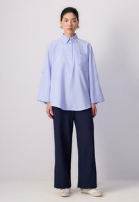 Cămașă cu dungi albastre deschise și guler, dotată cu un buzunar pe piept, asortată cu pantaloni largi negri închis și adidași albi. Material texturat, croi lejer.