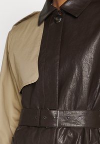 Zbliżenie na płaszcz wypożyczony z ciemno-brązowym skórzanym przodem oraz beżowym rękawem i panelem ramiennym.