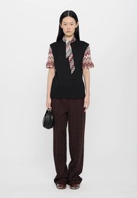 Μαύρη αμάνικη μπλούζα με γεωμετρικό σχέδιο κοντά μανίκια, σε συνδυασμό με σκούρο παντελόνι με ζιγκ ζαγκ σχέδιο. Μοντέλο κρατώντας μια μικρή μαύρη τσάντα.