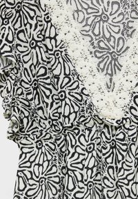 Tissu à motif floral noir et blanc avec une bordure en dentelle blanche texturée formant un V sur un tissu froncé.