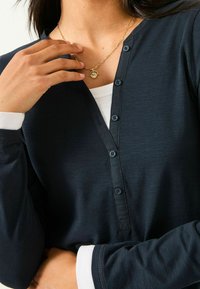 Navyblaues Langarmshirt mit Knopfkragen, aus strukturiertem Stoff und weißen Bündchen, getragen mit einer goldenen Anhängerkette.