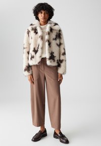 Faux furjas in crème met bruine sterachtige patronen, gecombineerd met tan wijde broek en donkere loafers. Zachte textuur en cropped ontwerp.