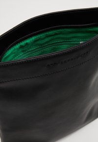 Borsa in pelle nera con una texture liscia e foderatura in tessuto verde. Presenta una tasca con zip all'interno e un logo del marchio impresso.