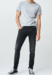 Camiseta gris de manga corta combinada con pantalones vaqueros negros ajustados y zapatillas altas negras. La tela parece suave, con un diseño casual y ajustado.