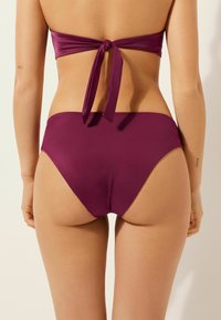 Bas de bikini en violet foncé, design taille haute avec texture lisse. Noué à l'arrière pour un ajustement réglable. Esthétique minimaliste.