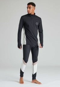 Schwarzes Langarm-Sportshirt mit weißen Seitenpanelen und Halb-Reißverschluss-Kragen, kombiniert mit schwarzen und weißen gemusterten Leggings. Glattes, dehnbares Material.