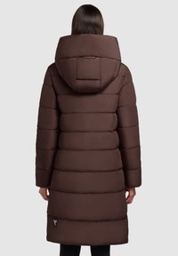 Manteau rembourré marron avec une grande capuche, un design matelassé et une texture remplie. Présente un accent noir près de l'ourlet. Design mi-long.