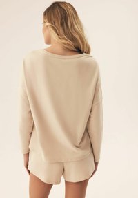 Beżowa bluzka z długim rękawem o luźnym kroju i okrągłym dekoltem, zestawiona z pasującymi szortami, wszystko z miękkiego materiału i minimalnymi detalami szycia.