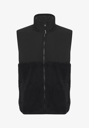 Zwarte vest met een hoge kraag, voorzien van een gladde bovenkant en een zachte, textuurrijke onderzijde. Middenvoor een rits en zijzakken.