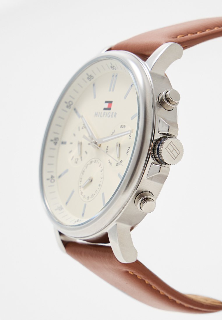 Silberner Metallarmbanduhr mit cremefarbener Zifferblatt, braunem Lederarmband und mehreren Ziffernblättern. Merkmale sind silberne Stundenziffern und ein Markenlogo.