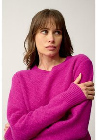 Pull en maille fuchsia avec un col rond, des poignets côtelés et une texture douce. Le design présente des manches amples pour un ajustement décontracté.