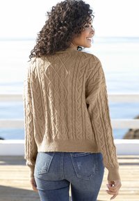 Beiger Kabelstrick-Pullover mit strukturiertem Muster, gerippten Bündchen und Saum. Kombiniert mit eng anliegenden blauen Jeans mit subtiler Ausbleichung.