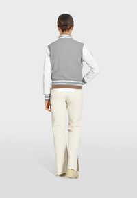 Gray and white bomber jacket with striped cuffs, back pockets, and cream pants with side slits, viewed from the back.