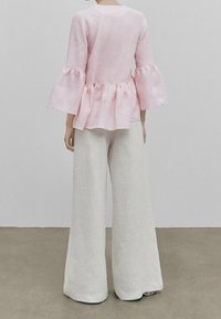 Haut rose clair à manches cloche avec une taille peplum associé à un pantalon blanc à jambes larges. Le tissu semble texturé et léger.