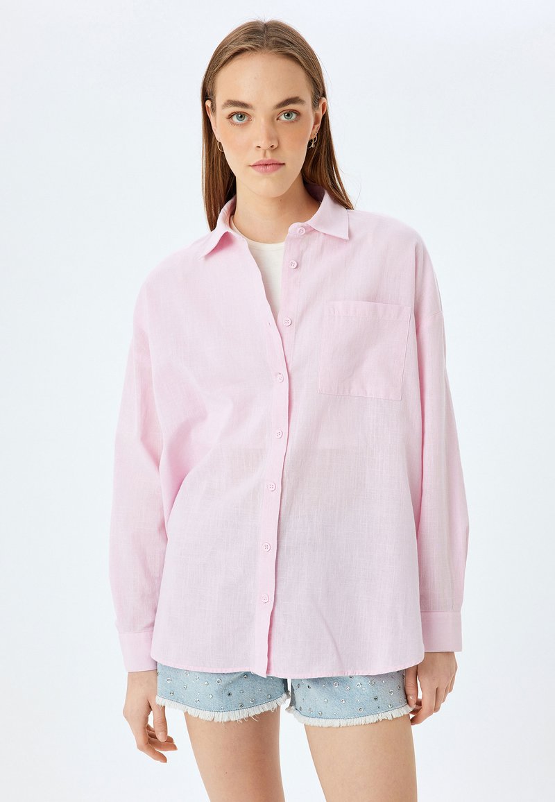 Camisa rosa claro de botones en un ajuste relajado, con un bolsillo en el pecho, mangas largas y una tela texturada parecida al lino.