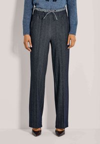 Donkergrijze wijde broek met verticale strepen, elastische tailleband en een trekkoord. Gepaard met een blauwe gebreide trui en puntige schoenen.